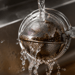 Stainless steel tea filter being cleaned under hot running water to remove tea residue and stains